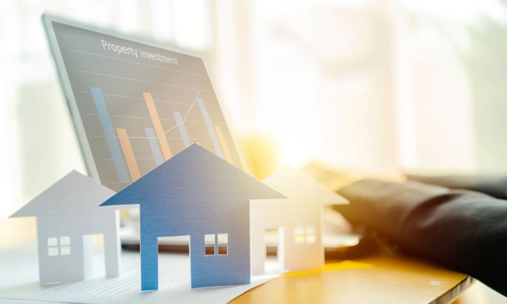 Hands typing on a laptop keyboard with overlay icons of house symbols, representing real estate technology.