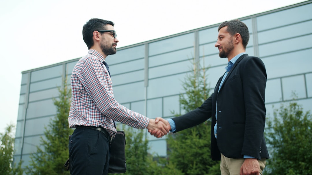A firm handshake between two well-dressed individuals in front of a beautiful modern house, signifying a trusted real estate partnership.