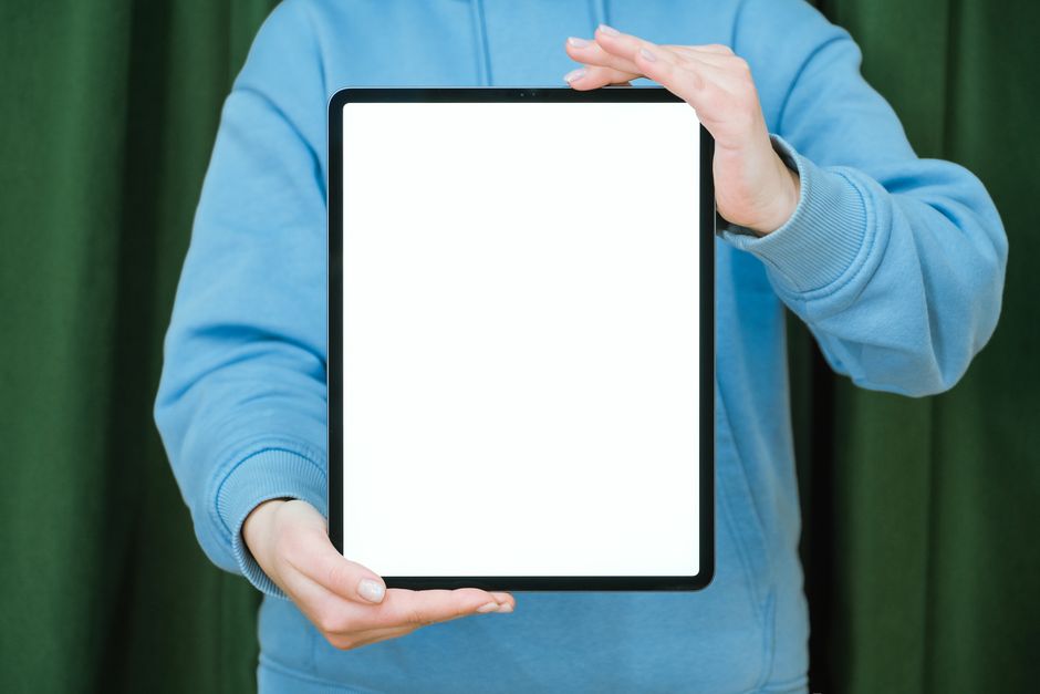Close-up of a person's hands holding a digital tablet that displays the interior of a bright, modern home, symbolizing the...