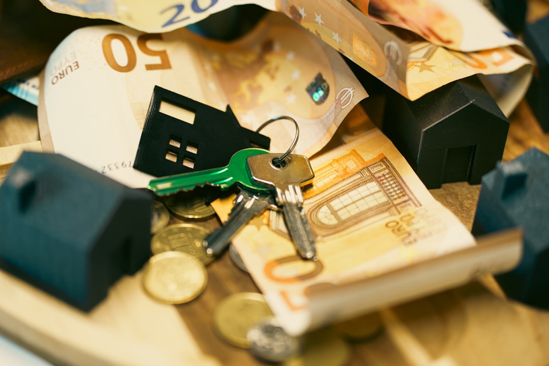 A person's hands signing a real estate contract on a clean desk next to a set of house keys and a calculator, illustrating the financial and legal aspects of a property transaction.