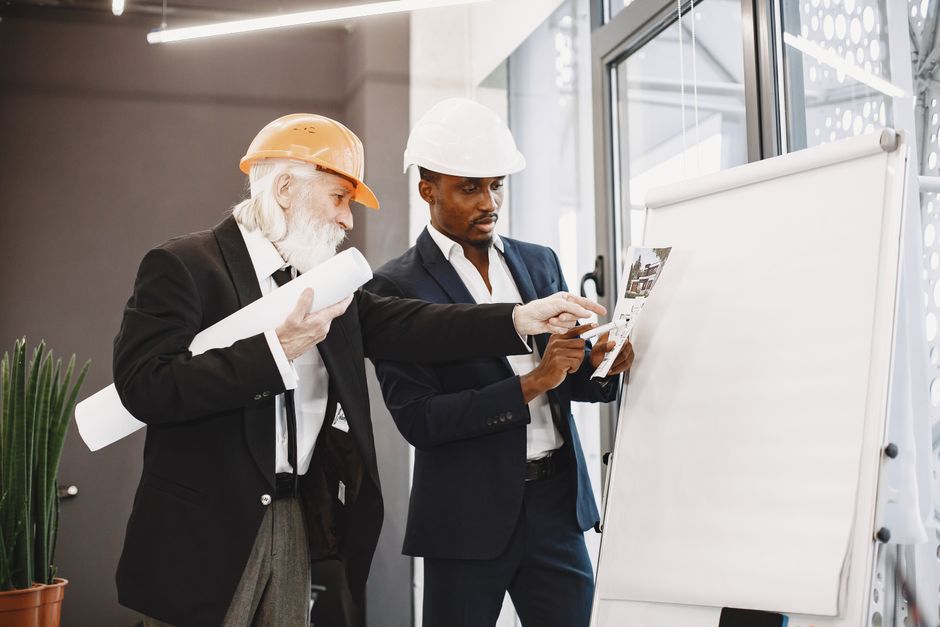 A real estate agent and a client stand in a bright, modern kitchen, professionally dressed, discussing architectural blueprints, representing expert guidance in the home buying process.