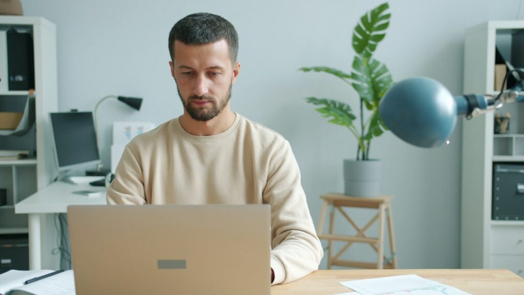 Rental property owner sits at a clean, modern desk in a brightly lit home office, focused on their laptop while building t...